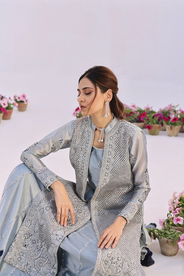  Step into elegance with Fiza by Mona Imran, crafted from luxurious lambha tissue with mesmerizing cutout pattern jaal adorned with pearls and diamonte work.