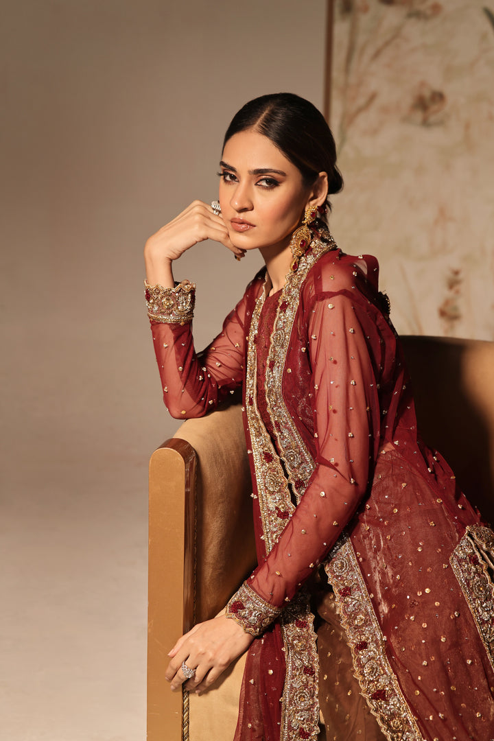  Step into timeless elegance with Gulabposh by Mona Imran, featuring a deep maroon kora net jacket adorned with exquisite antique gold appliquéd borders.